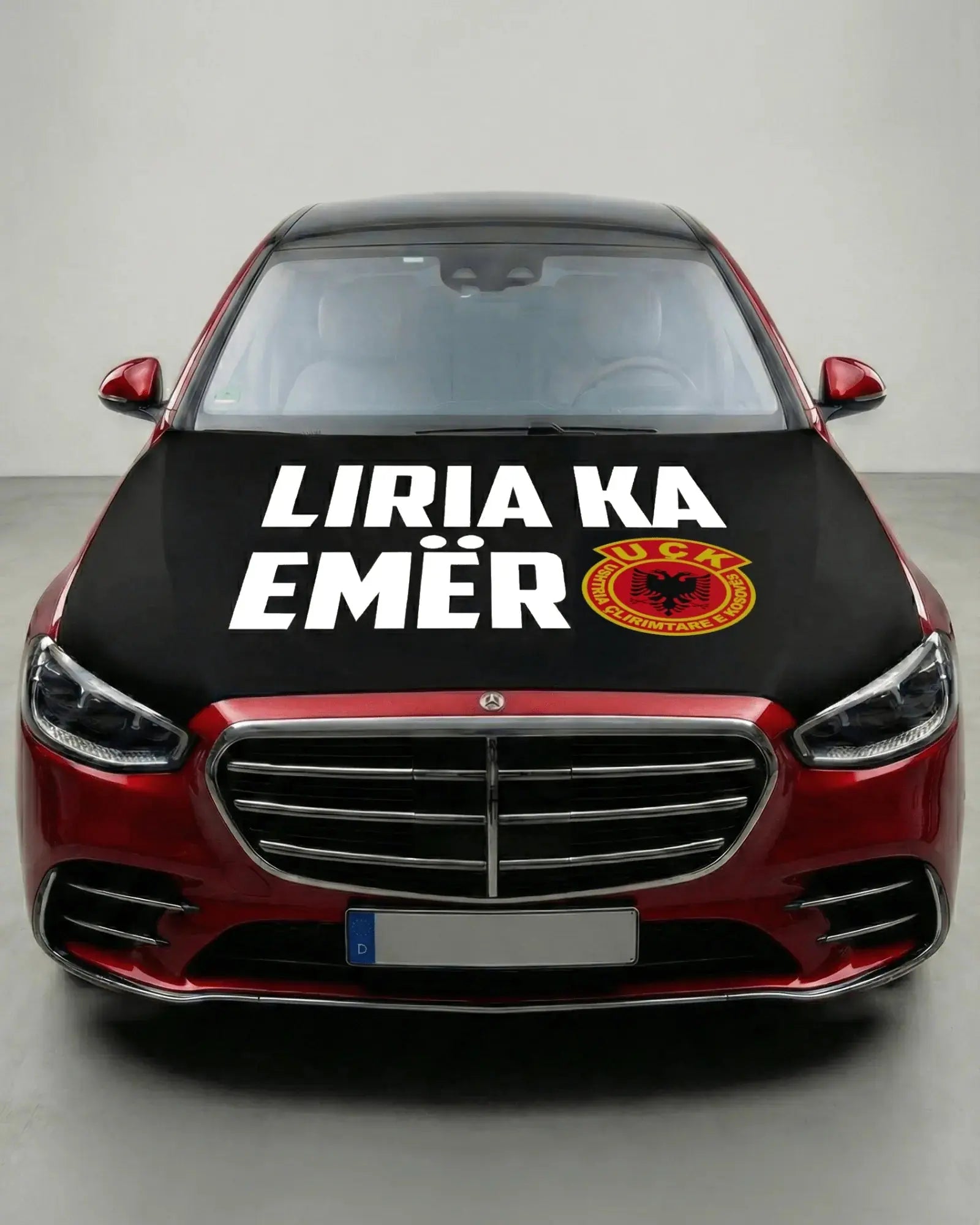 Schwarze UÇK Motorhaubenflagge auf Auto montiert, mit weißem Text "Liria ka emër" und UÇK Wappen für Autokorso
