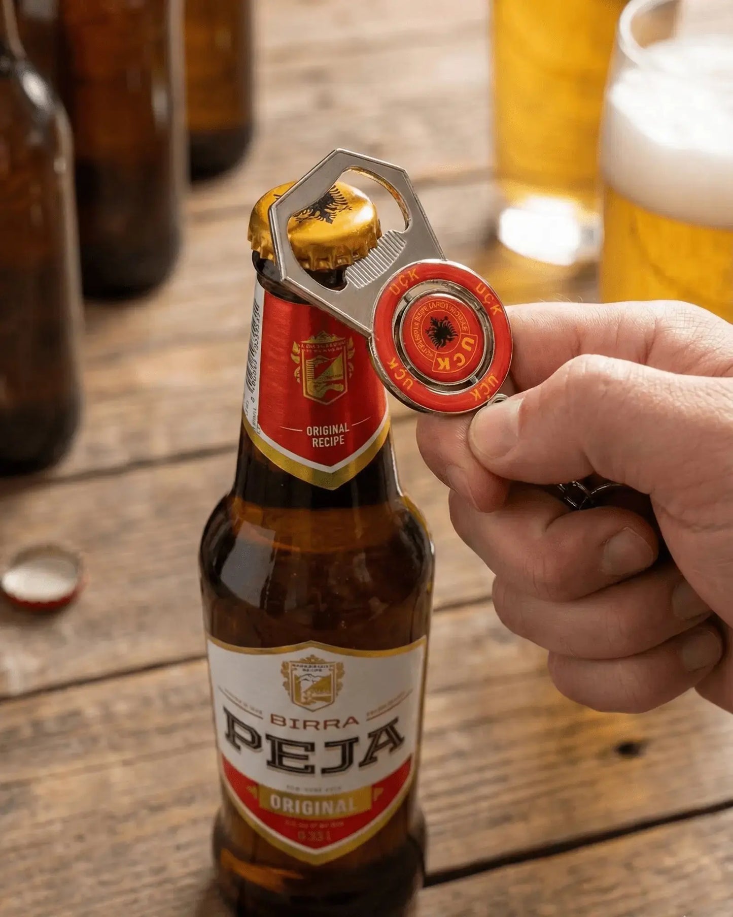 UÇK Flaschenöffner öffnet eine Flasche Birra Peja, Schlüsselanhänger mit drehbarem UÇK Emblem aus Metall